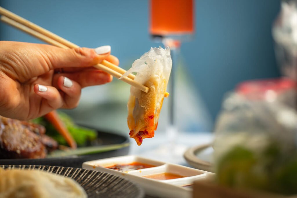 Gyoza lifted with chopsticks beside a cocktail at Titu, Mayfair