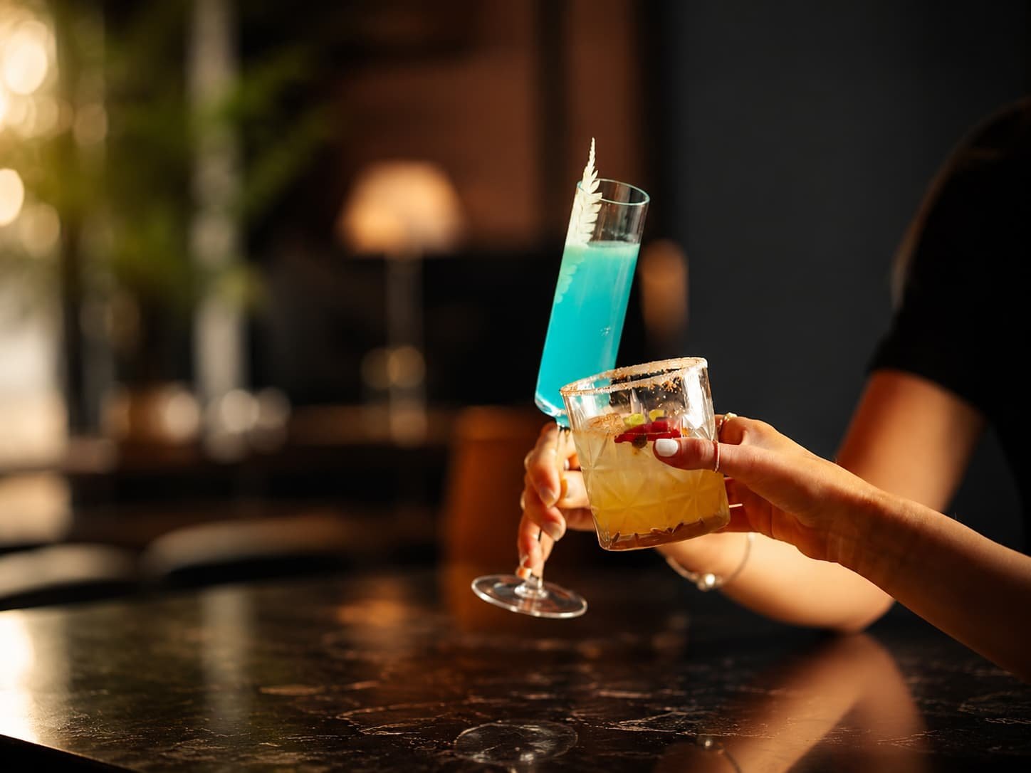 Hands raising blue and citrus cocktails in a cocktail bar in London
