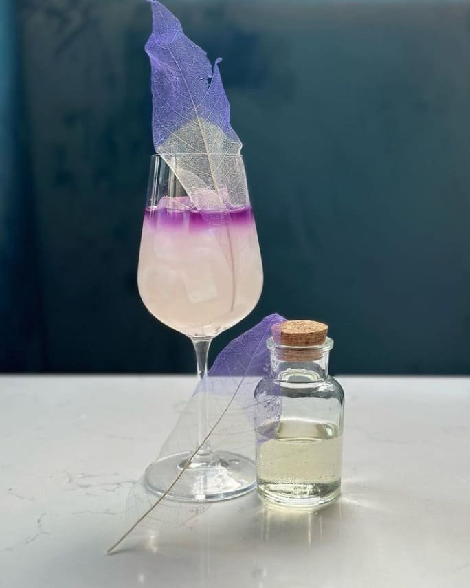 Layered purple cocktail with infusion bottle at Titu London cocktail bar