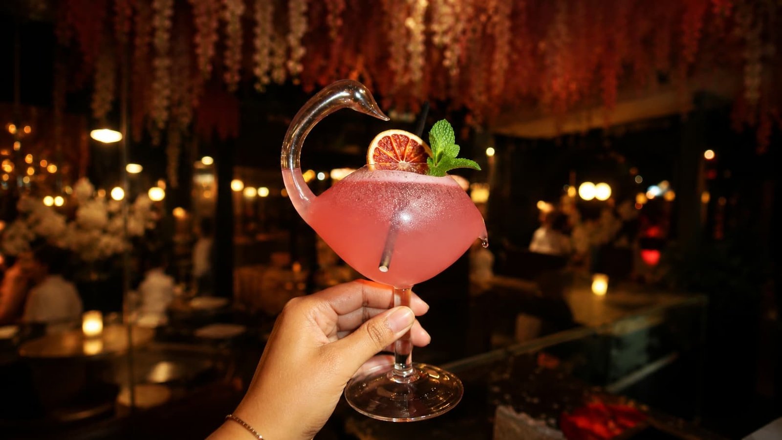 Pink non-alcoholic cocktail in a swan-shaped glass with citrus and mint garnish.